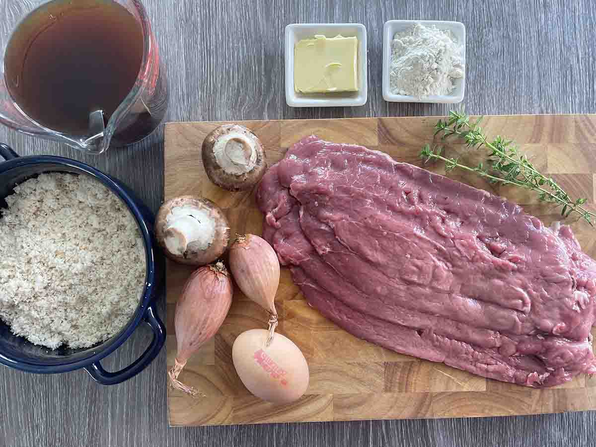 ingredients on a board including thin sliced beef, egg, shallots, butter, flour, mushrooms, stock and breadcrumbs.