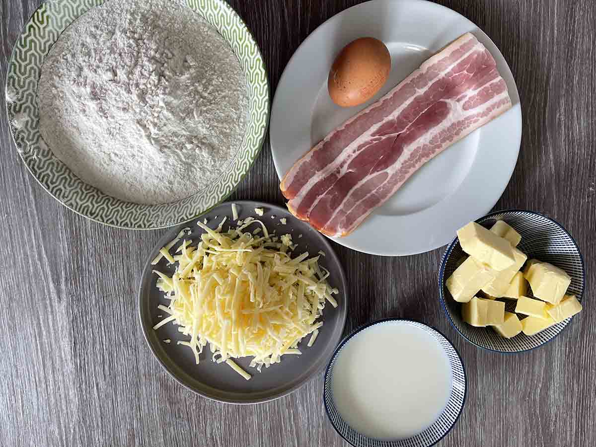 ingredients on plates including bacon, eggs, cheese, flour, butter and milk.