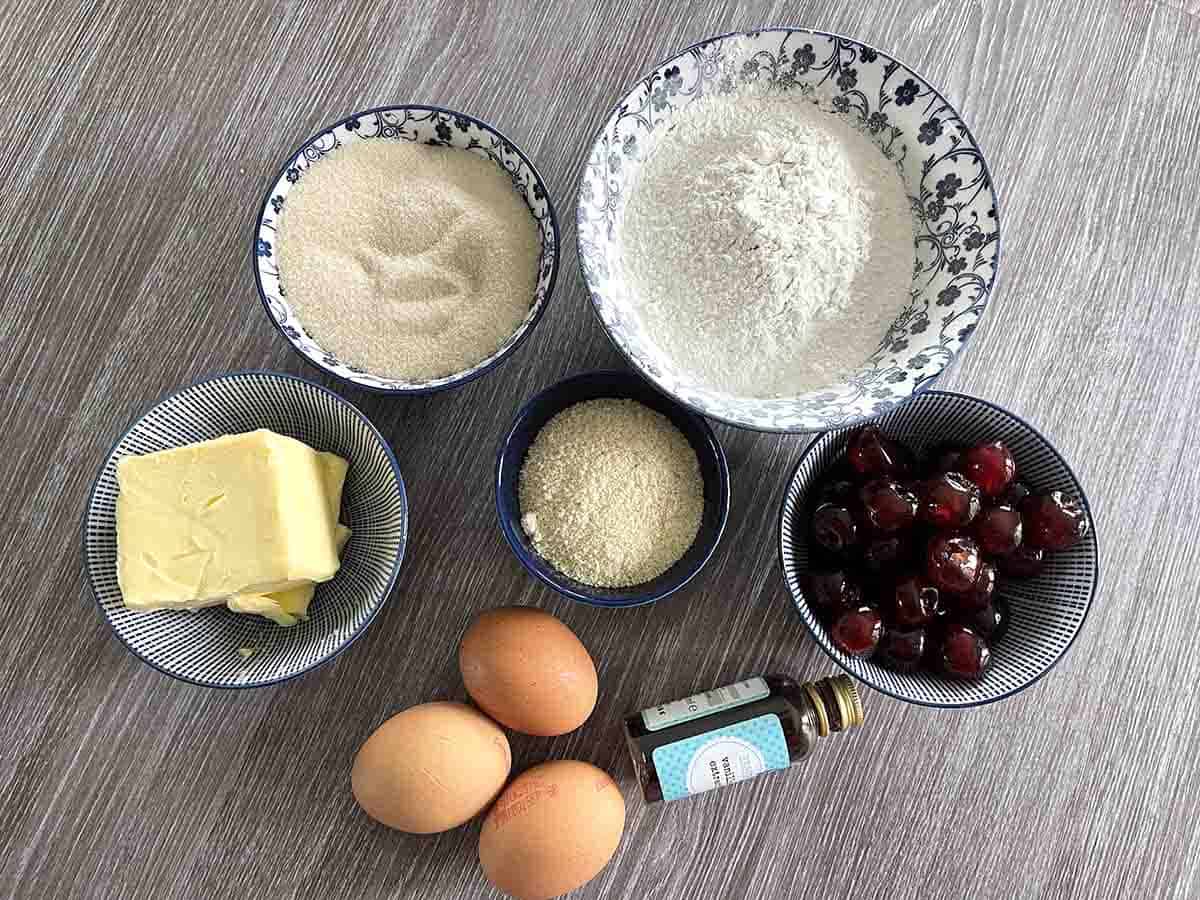 ingredients in bowls including, flour, cherries, eggs, vanilla, butter and sugar.