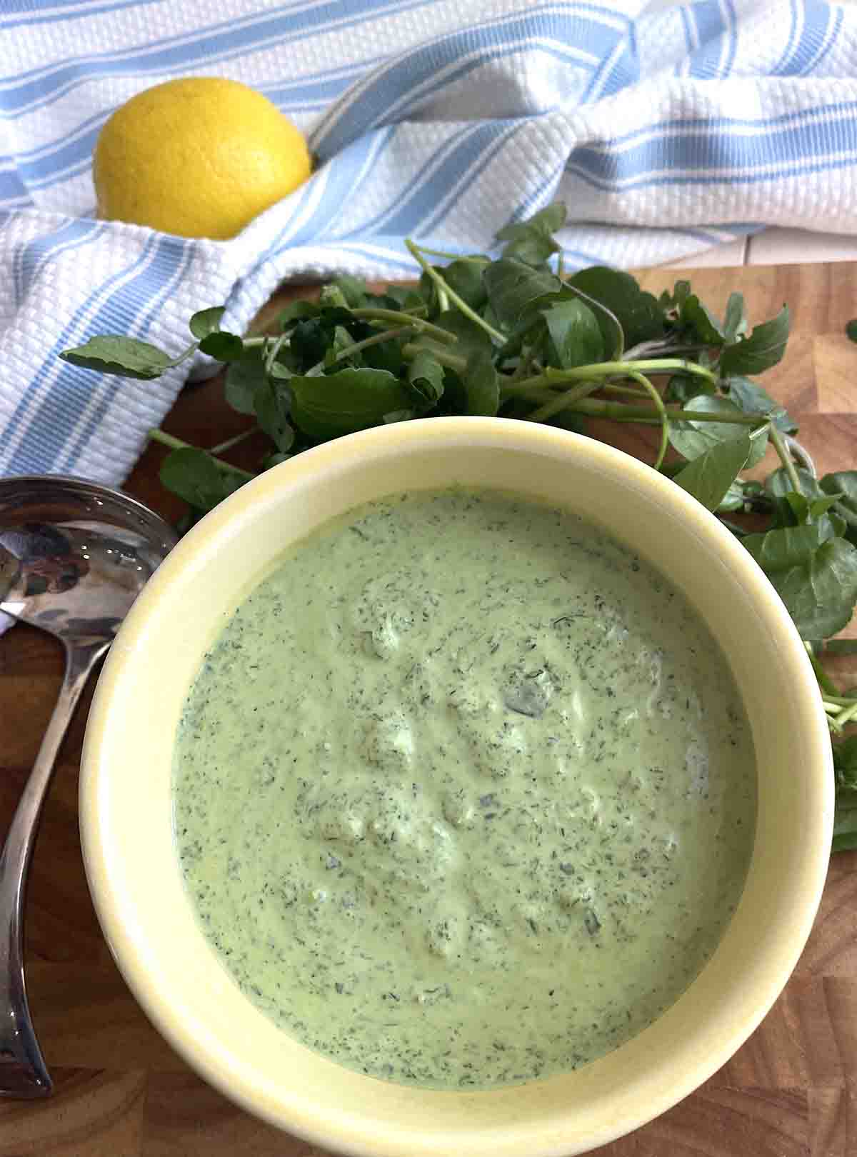 watercress sauce in a bowl with a lemon and watercress in the background.