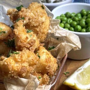 cod cheeks in panko in a wire dish with peas and lemon to the side.