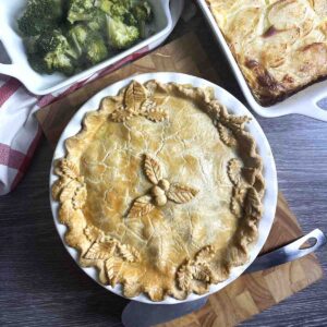 turkey and ham pie with dish of broccoli and potatoes at the top.
