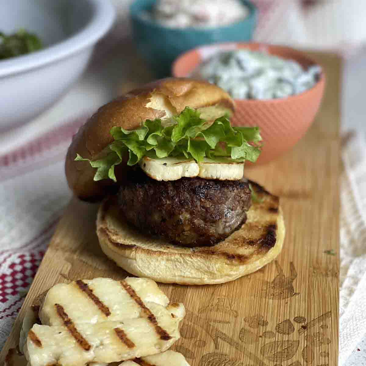 Minted lamb burger in a bun with halloumi on a board.