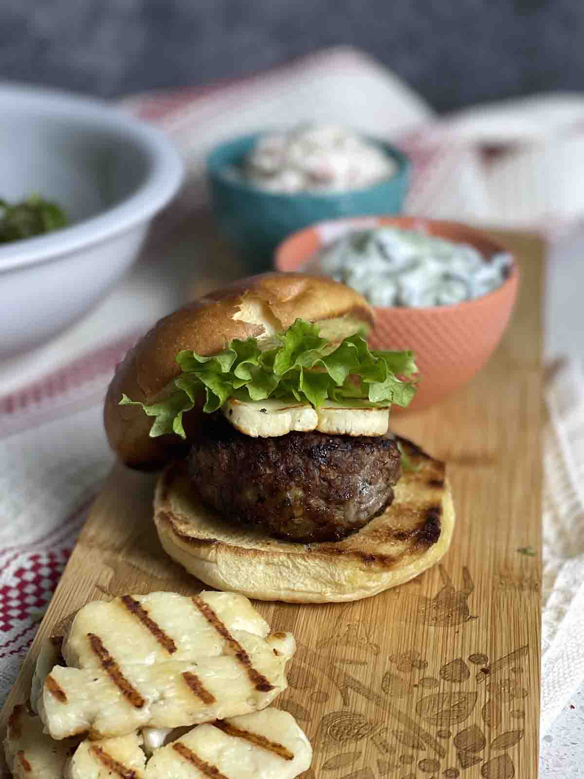 Minted lamb burger in a bun with halloumi on a board. 