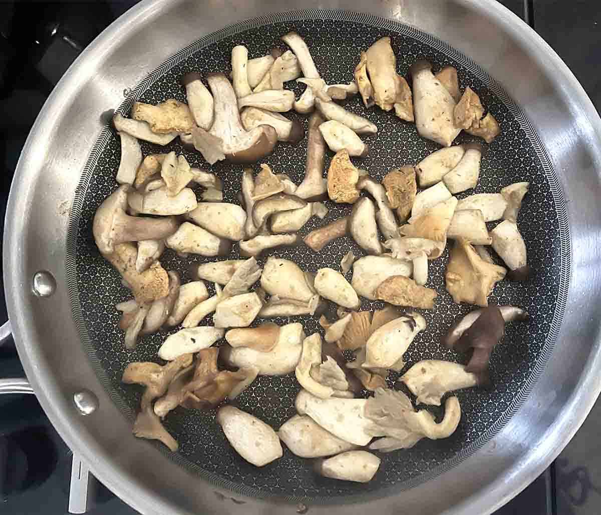sliced mushrooms cooking a frying pan.