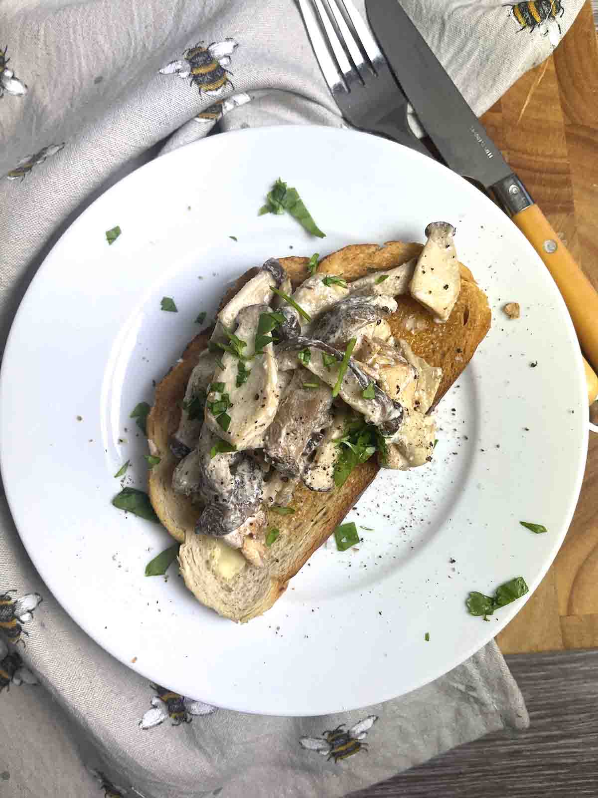 Creamy mushrooms on toast on a white plate with cutlery to the side.s