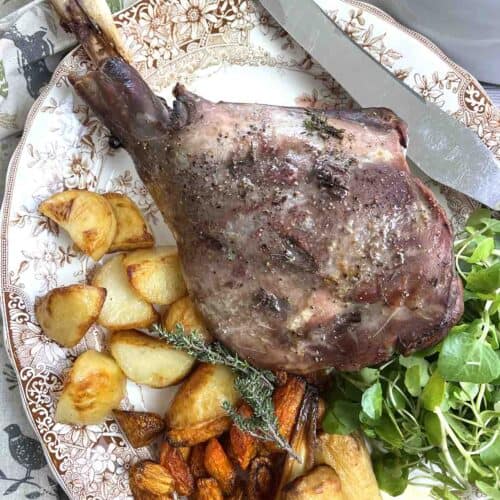 roast venison haunch on a plate with vegetables.