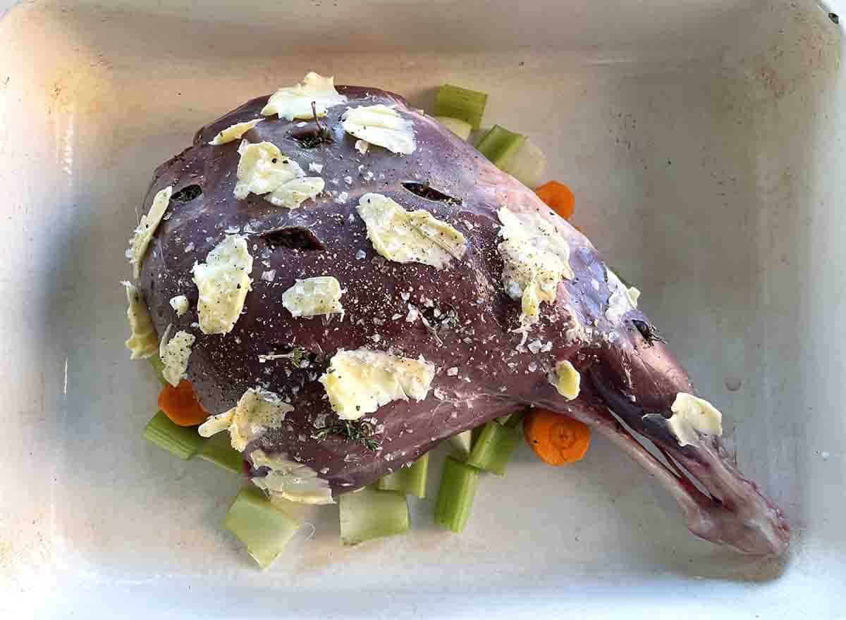 venison leg stuffed with thyme and smeared with butter on vegetables in the roasting dish.