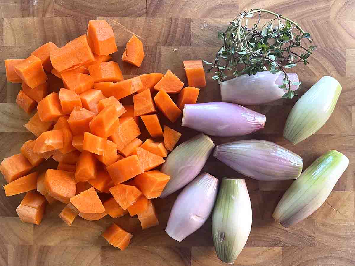 peeled and chopped carrots and shallots on a board.