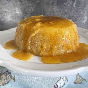 microwave sponge pudding on a plate with syrup falling down the sides.