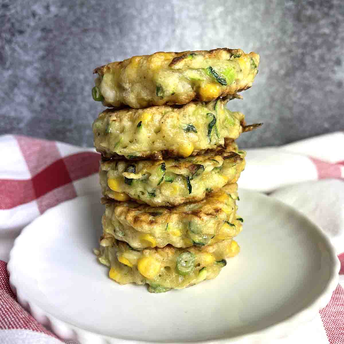 courgette nd sweetcorn fritters stacked on a plate.