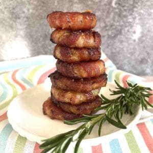 Bacon wrapped onion rings stacked on a plate.