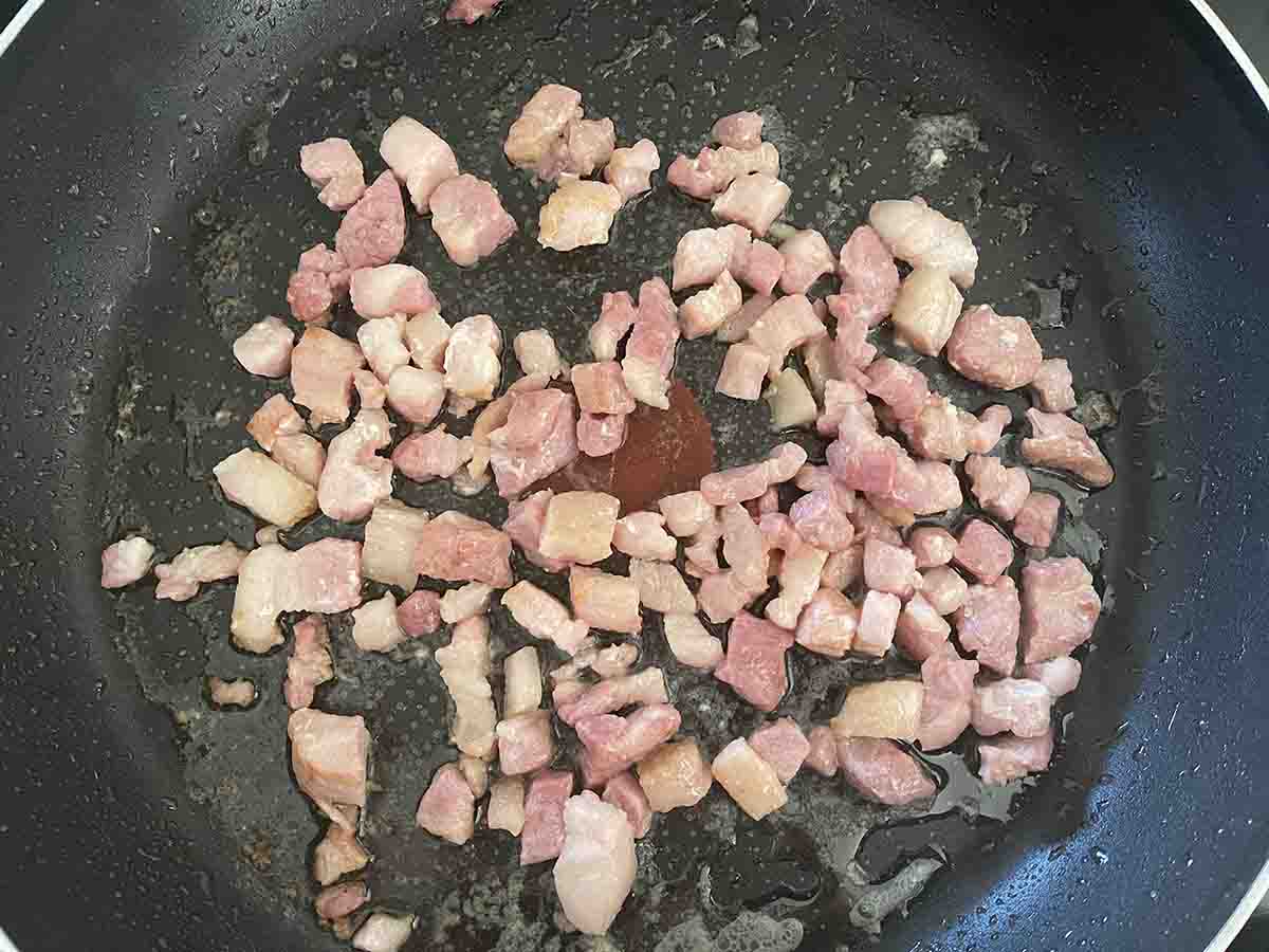 bacon lardons frying in a pan.