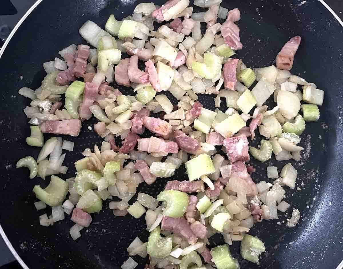 vegetables and bacon frying in a pan.